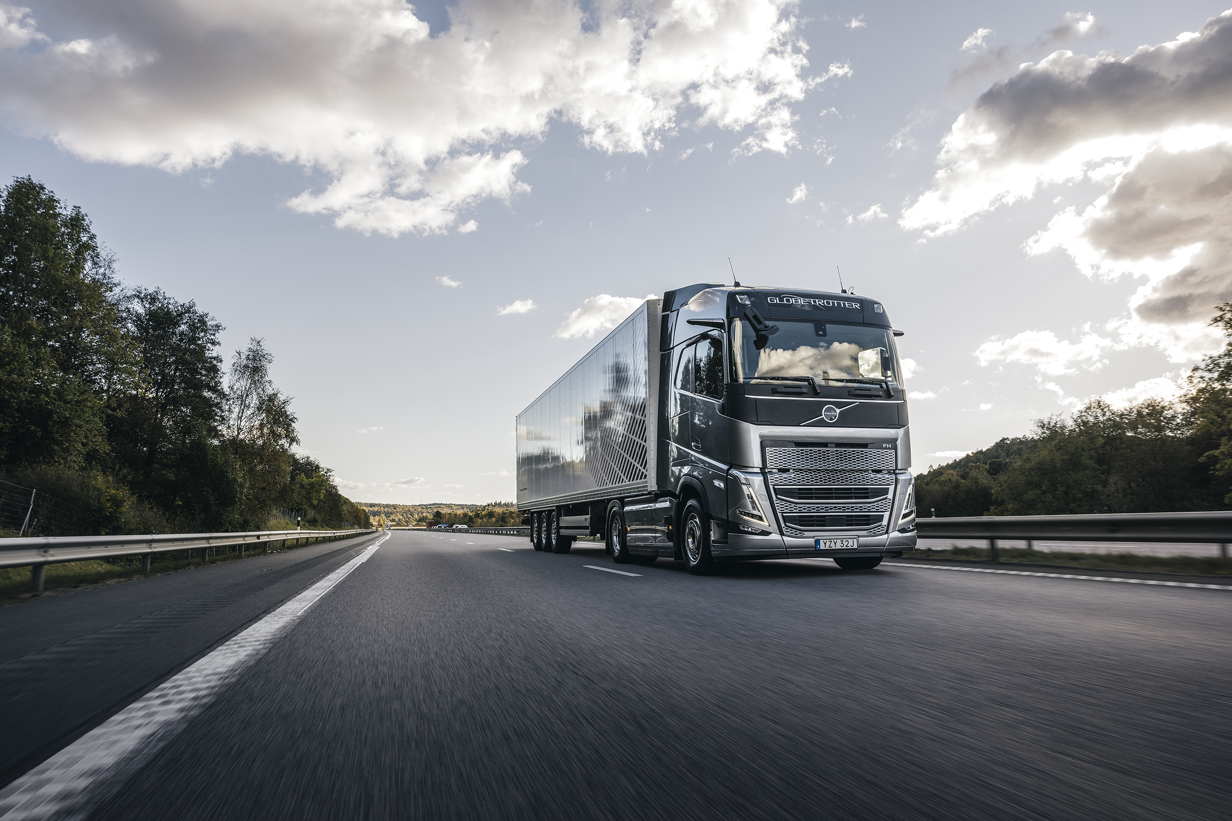 A green and silver colored Volvo truck is driving on a highway